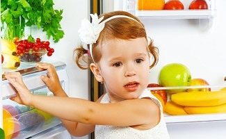 happy little girl near the fridge with healthy foods, fruits