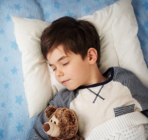 six years old child sleeping in bed on pillow with alarm clock and a teddy bear