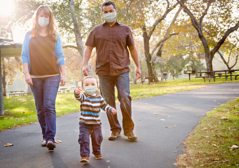 Happy Mixed Race Ethnic Family Walking In The Park Wearing Medical Face Mask