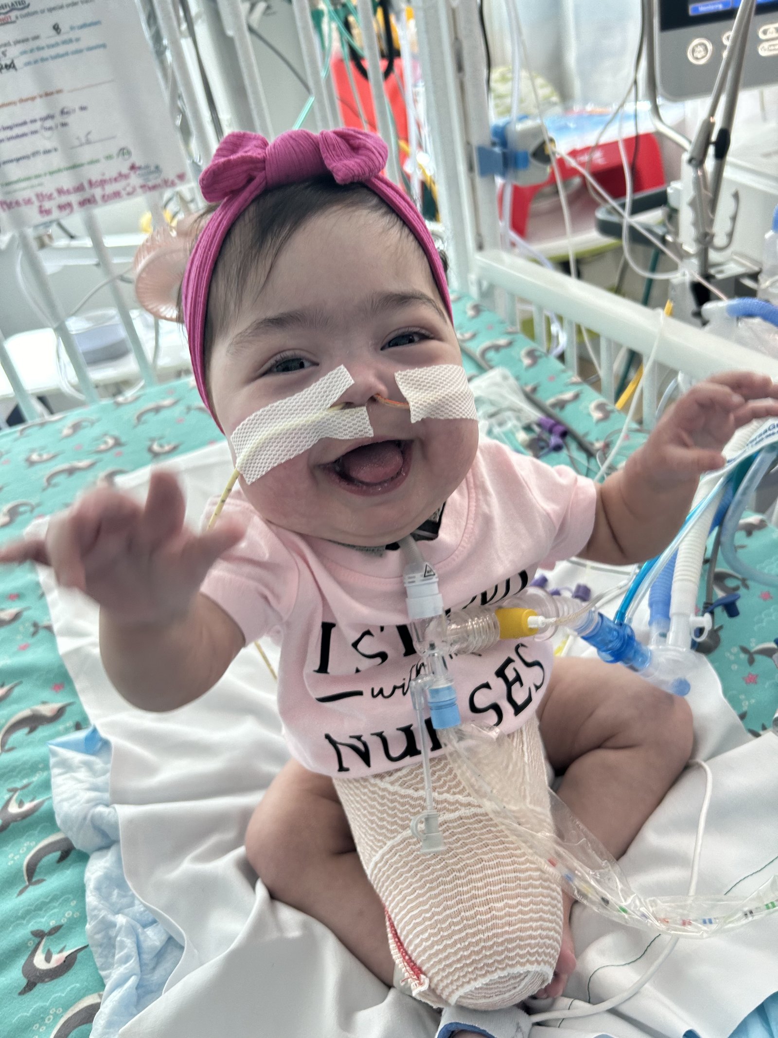 Baby Lynlee grinning in a pink 'I Sleep with Nurses' onesie with a pink bow