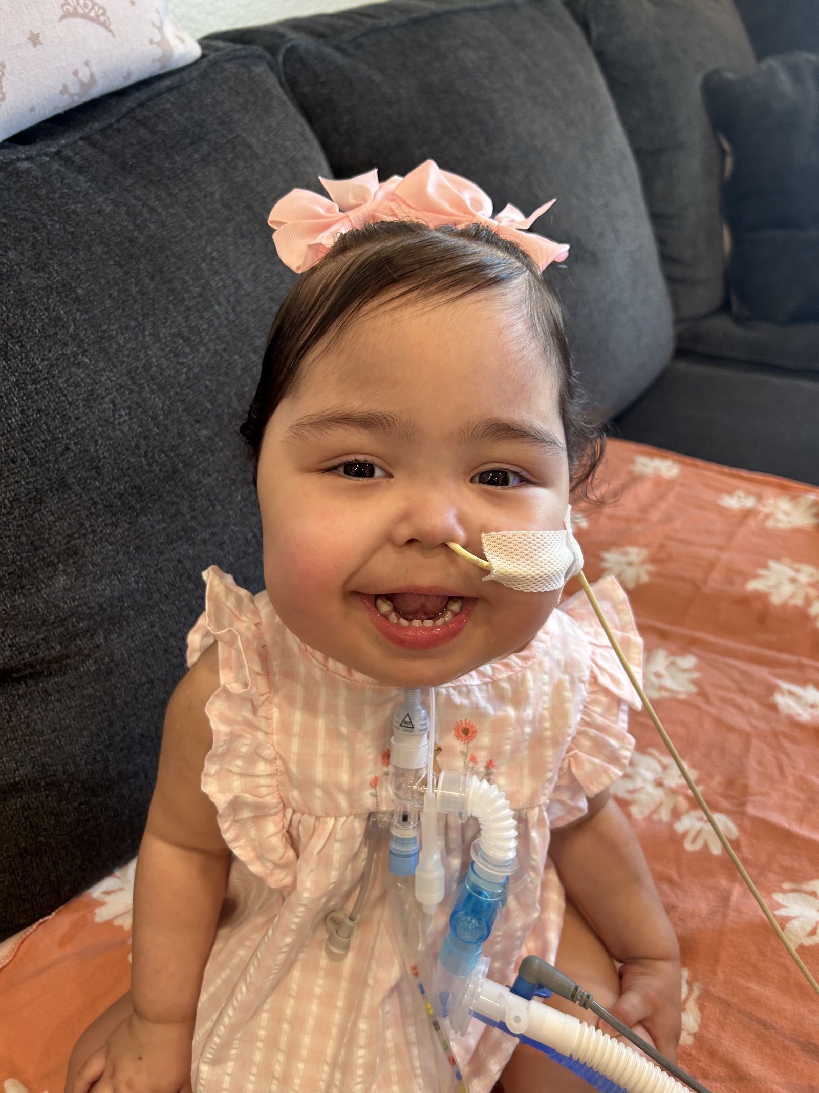 Toddler Lynlee at home on the couch in pink bows, smiling brightly