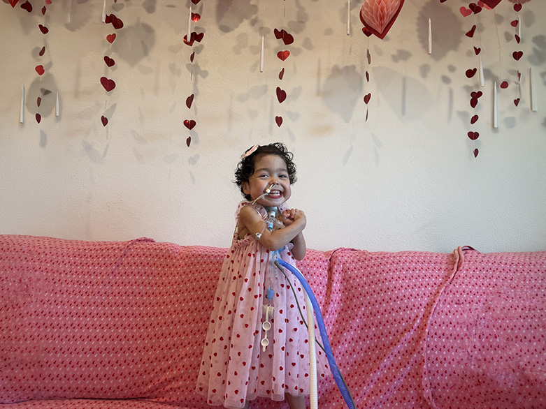 Lynlee at age 2, smiling in a pink heart-print dress on Valentine's Day