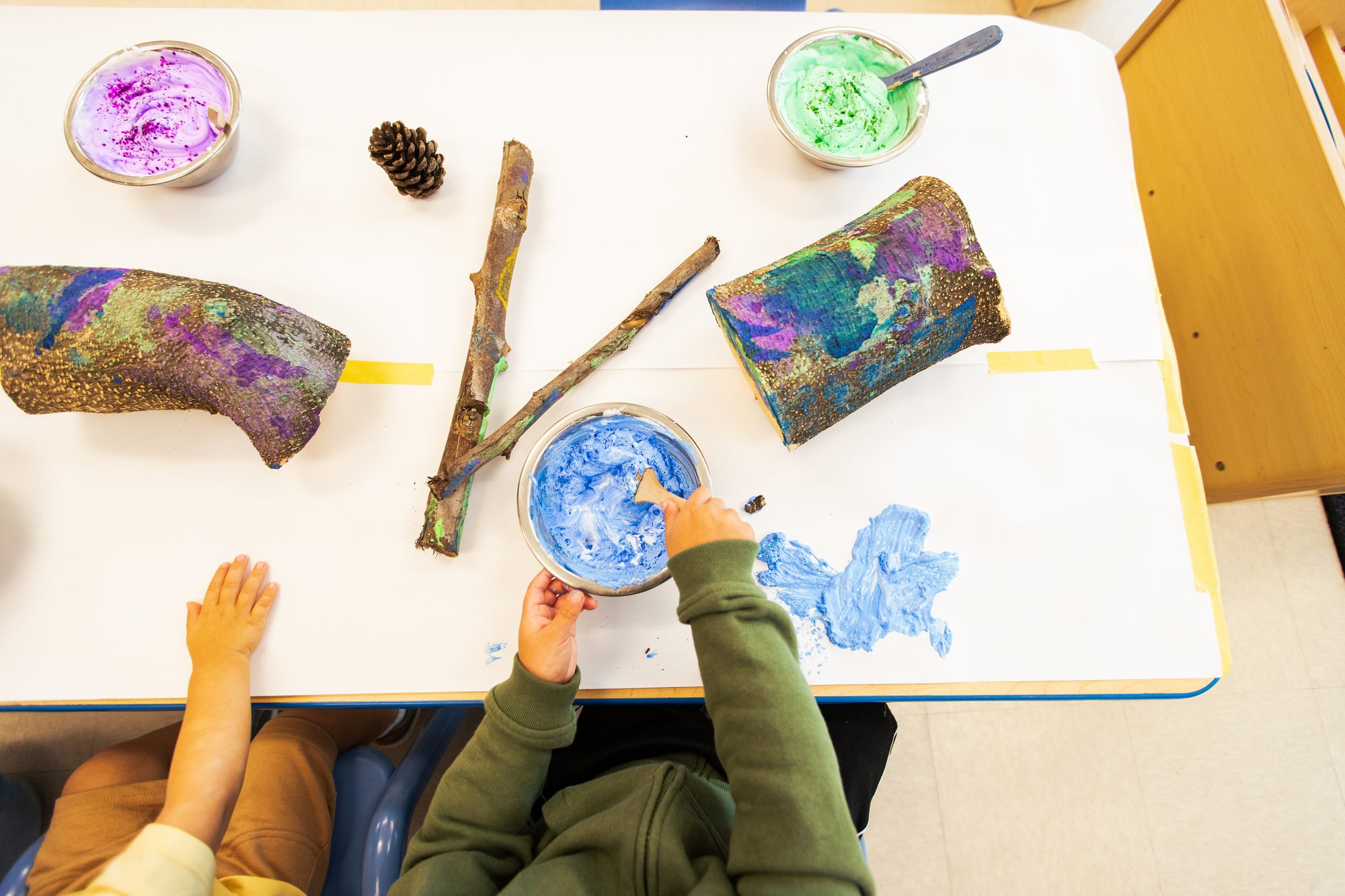 Preschooler painting a tree branch at Alexa's PLAYC