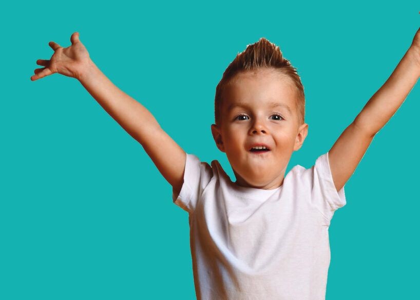 A young child smiling with arms raised in the air